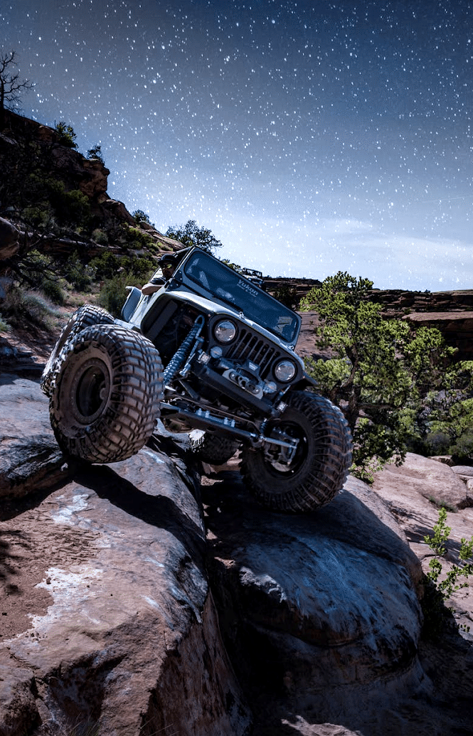 Jeep climbing a rocky terrain under a starry night sky.