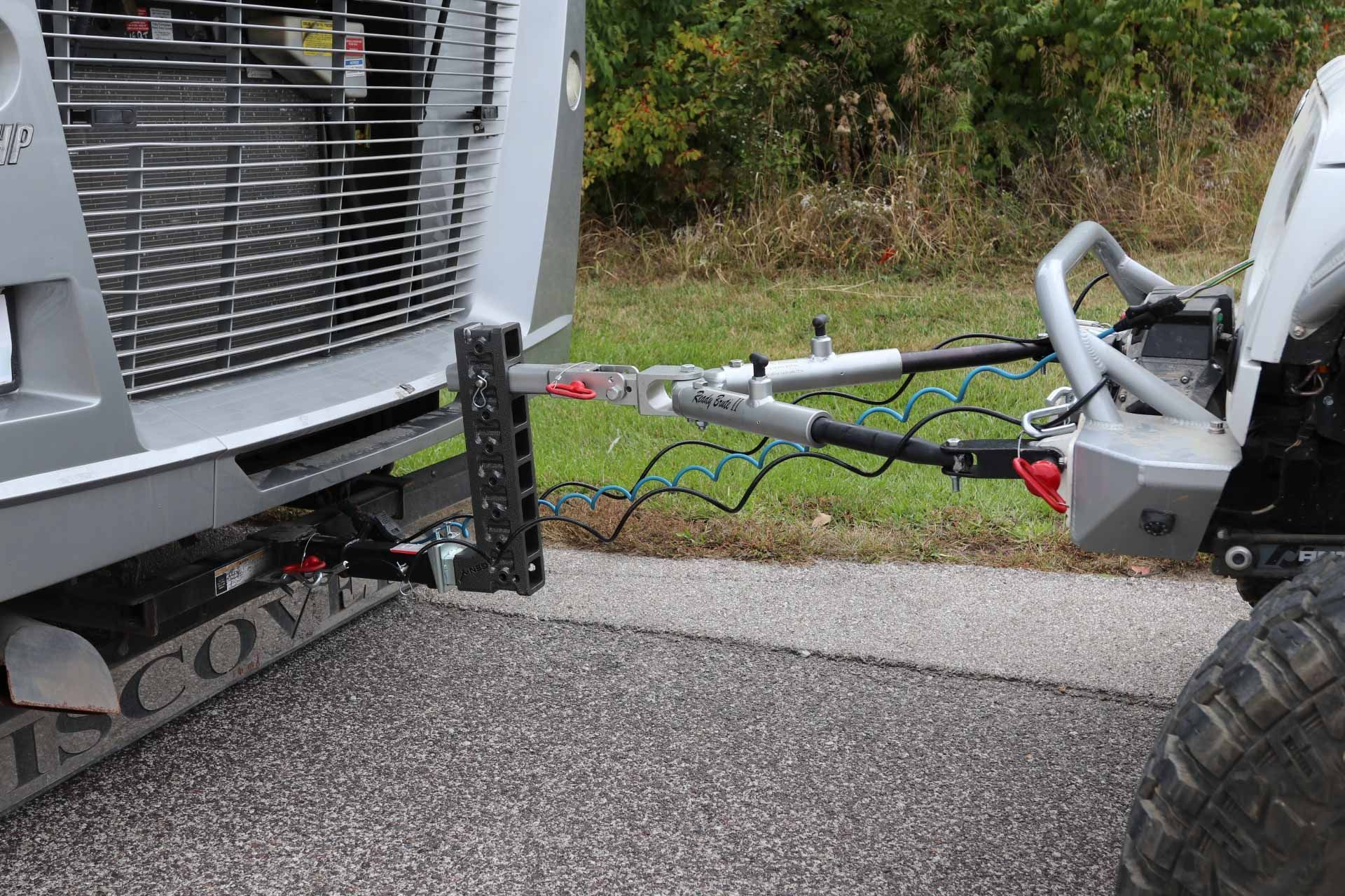 A silver truck towing a gray Jeep with a tow bar on asphalt road outdoors.