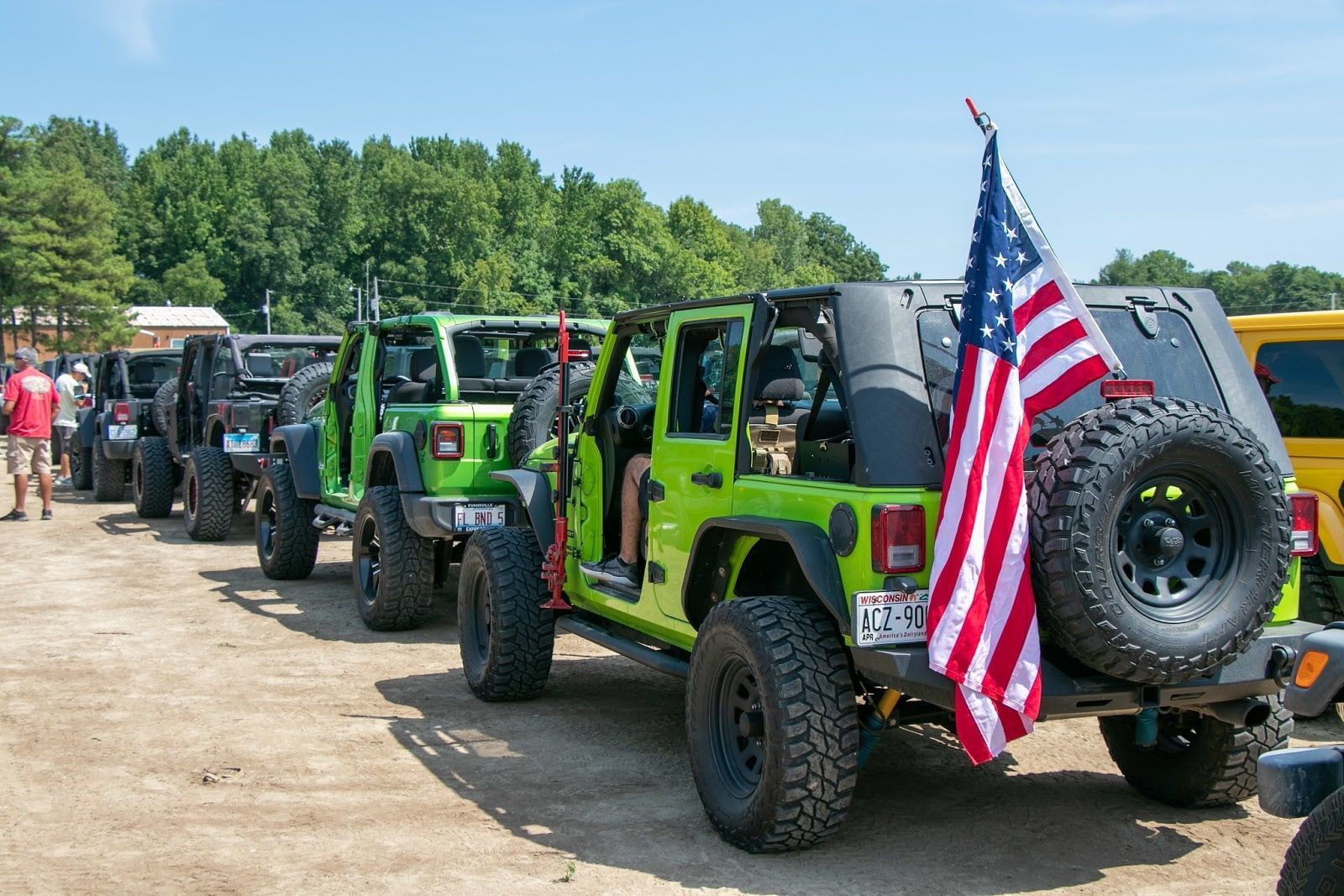 Line of brightly colored Jeeps, green and black, with an American flag attached to the back of the lead vehicle.