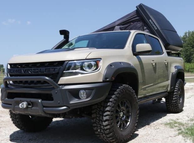 Tan Chevrolet Colorado pickup truck modified for off-road, roof-mounted tent, black accents.