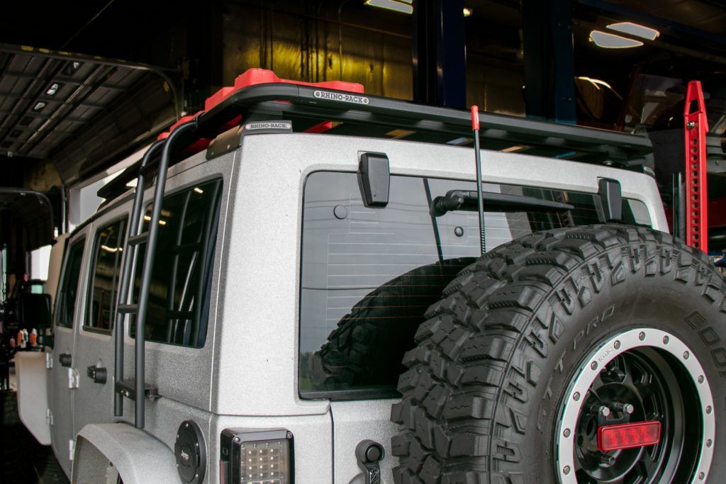A white utility vehicle equipped with a black roof rack system and red accent accessories.