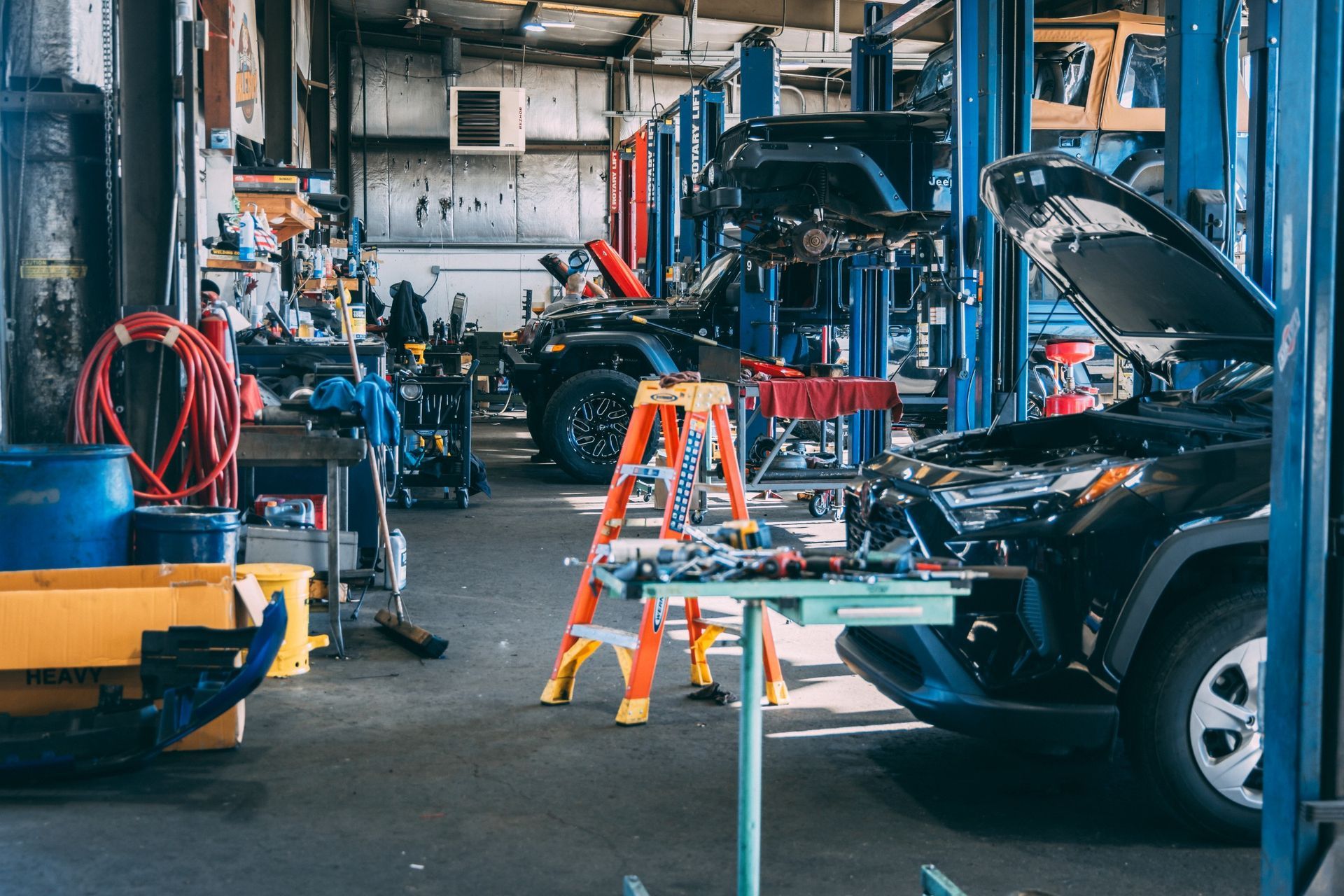 Multi-bay automotive workshop interior with blue steel support columns, blue and red hydraulic