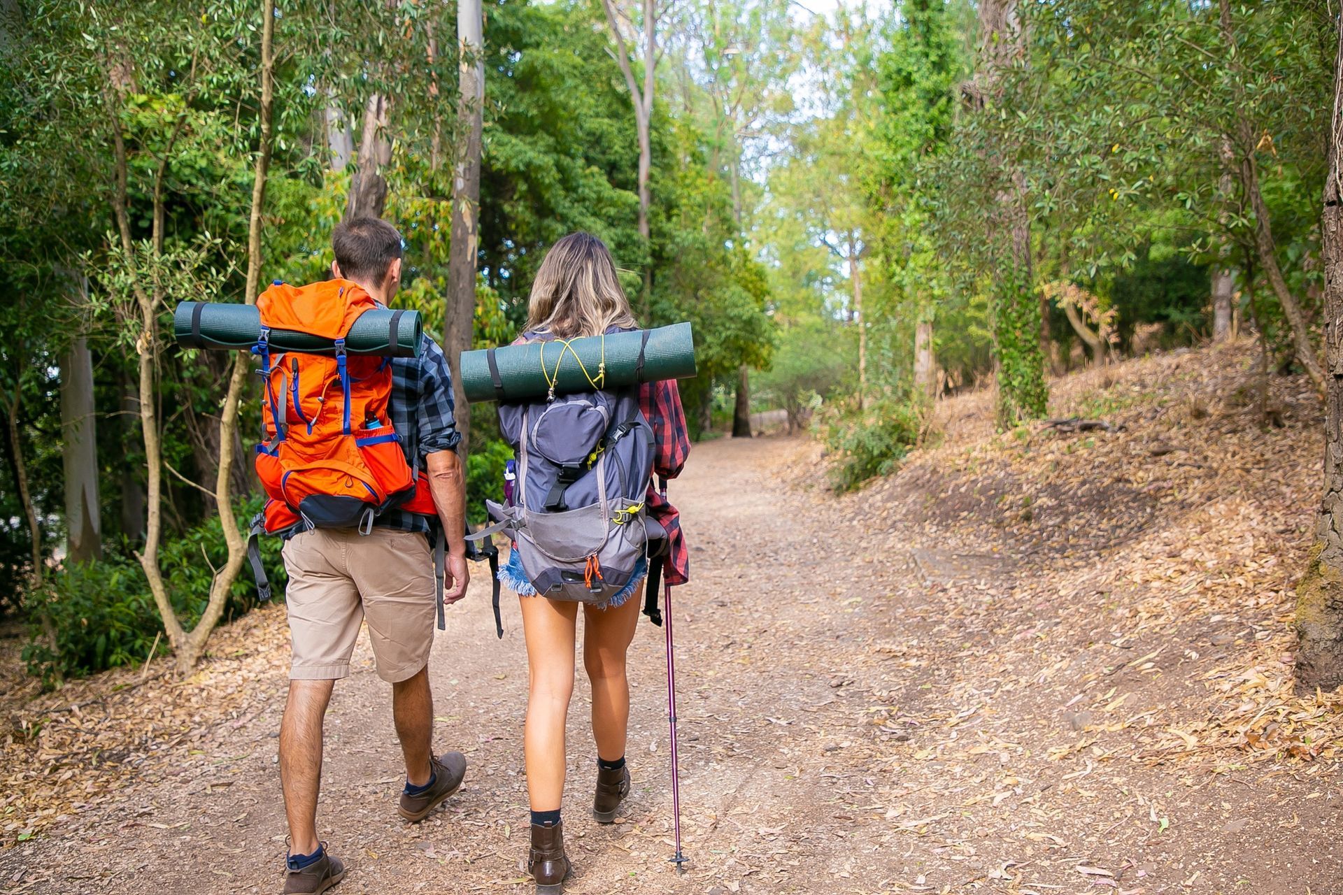 A man and a woman with backpacks are walking down a path in the woods.