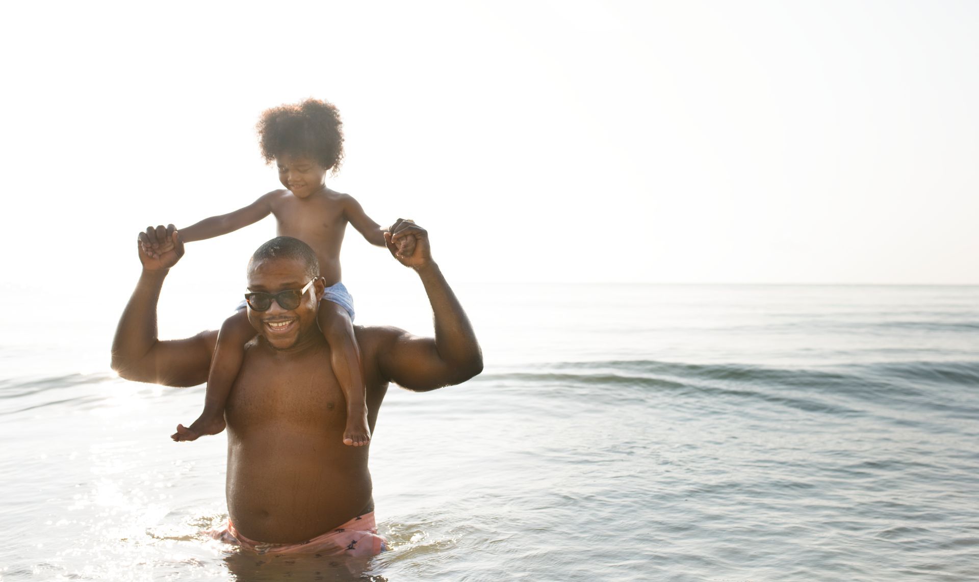 A man is carrying a little girl on his shoulders in the ocean.