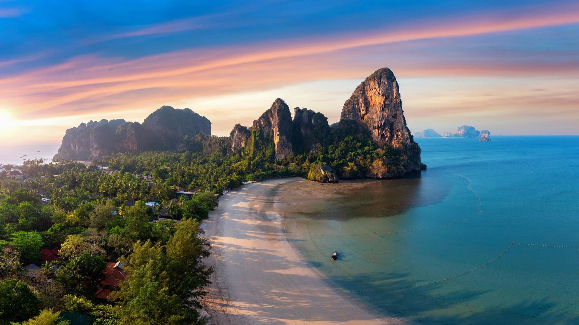 An aerial view of a tropical beach with a mountain in the background at sunset.