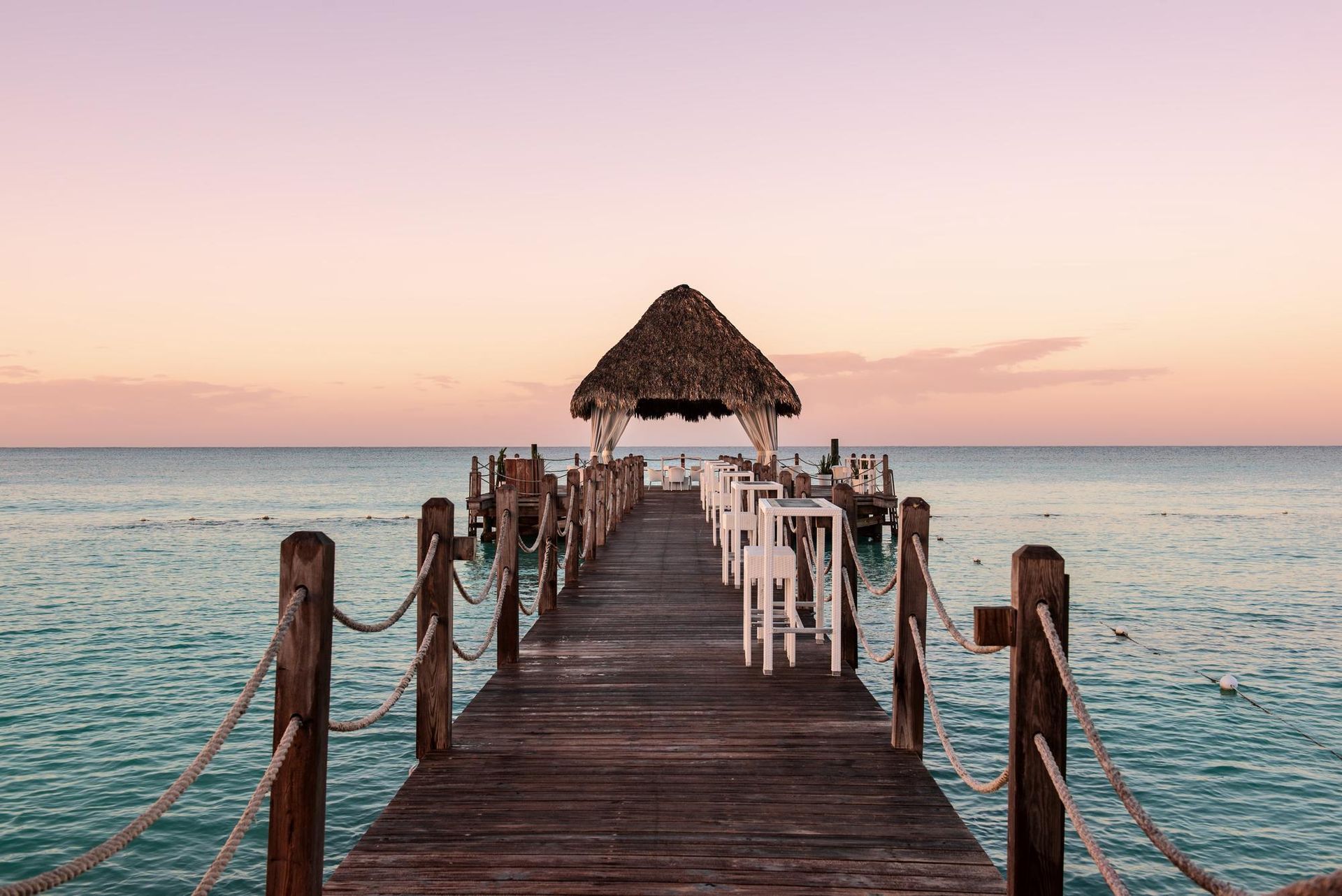A wooden dock leading into the ocean at sunset.