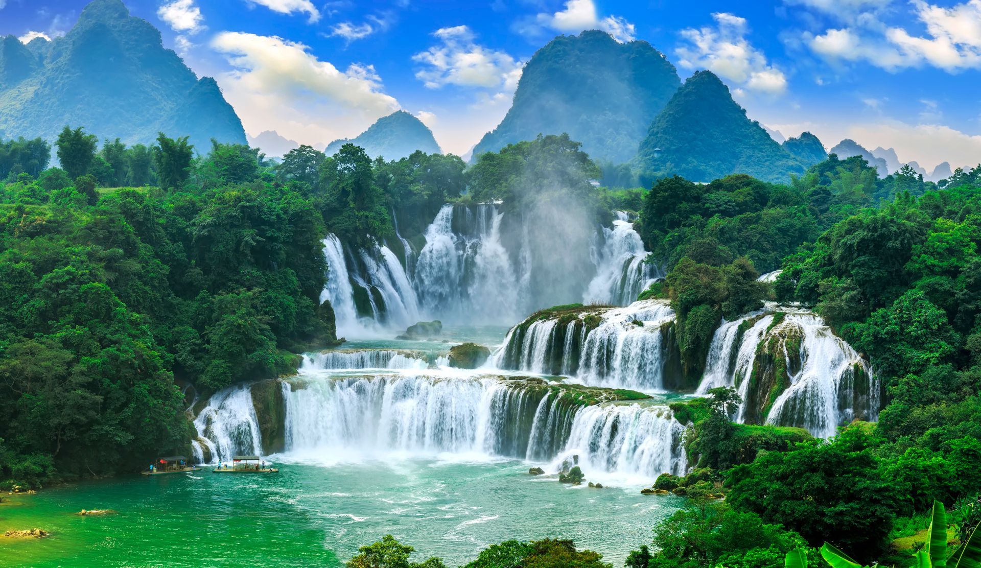 A waterfall in the middle of a forest with mountains in the background.