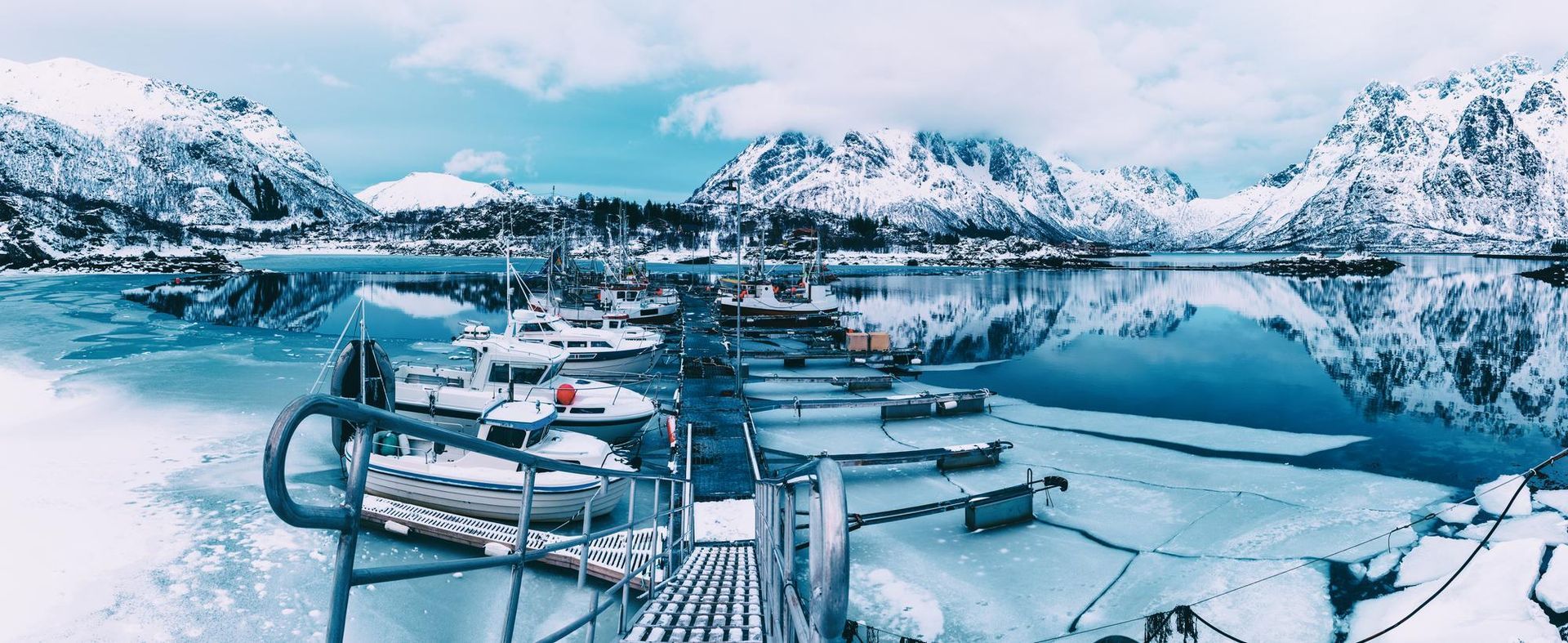 A dock with boats docked in the snow with mountains in the background.
