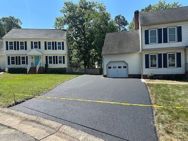 Freshly paved black asphalt driveway in front of suburban homes, showcasing smooth surface.