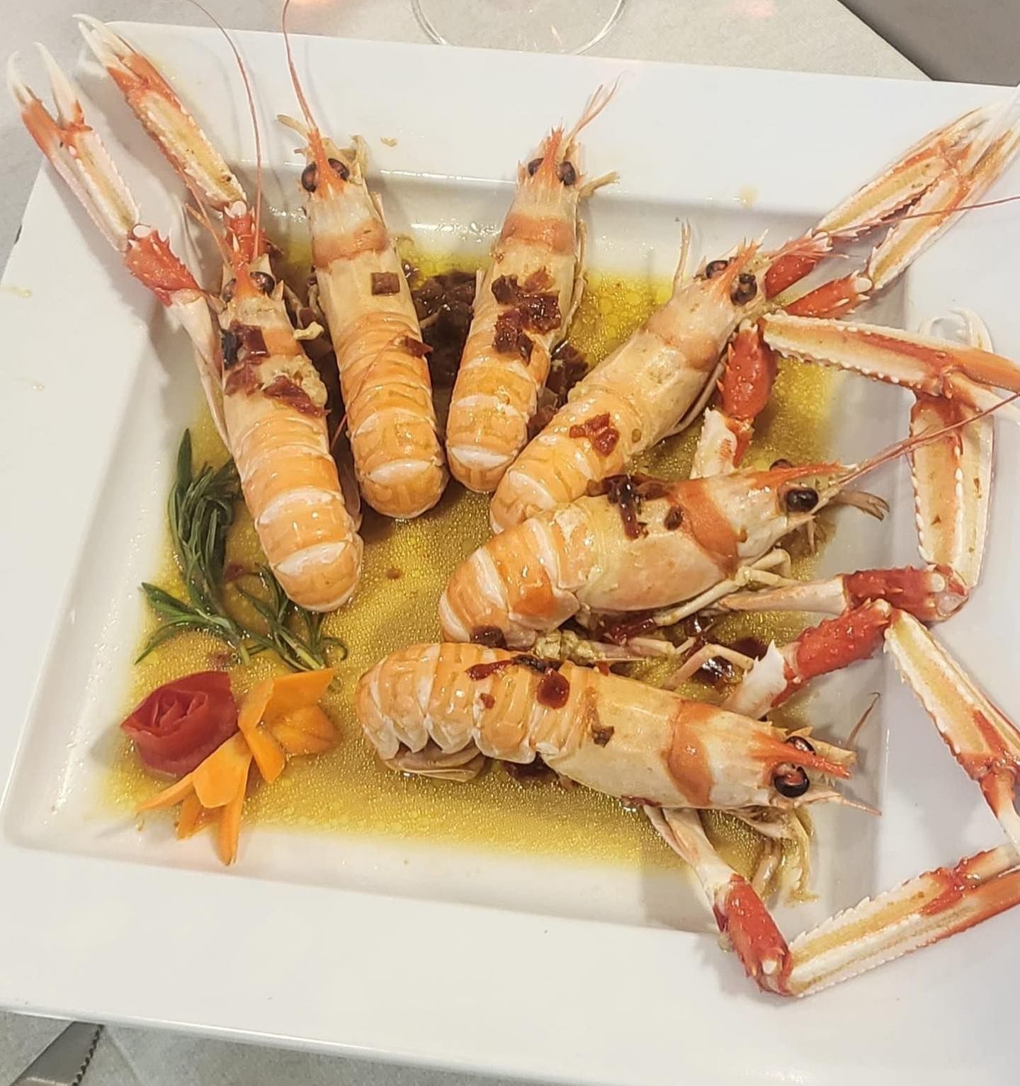 Scampi cotti serviti su un piatto quadrato bianco con contorno e salsa.