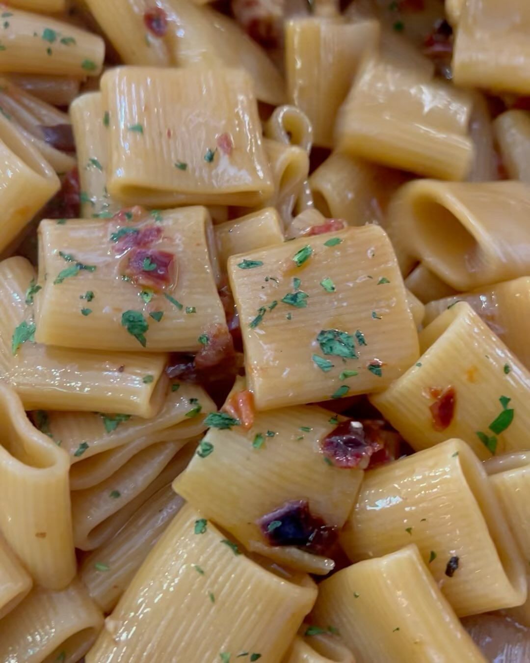 Primo piano di pasta rigatoni condita con salsa, guarnita con erbe aromatiche e piccoli pezzetti rossi.