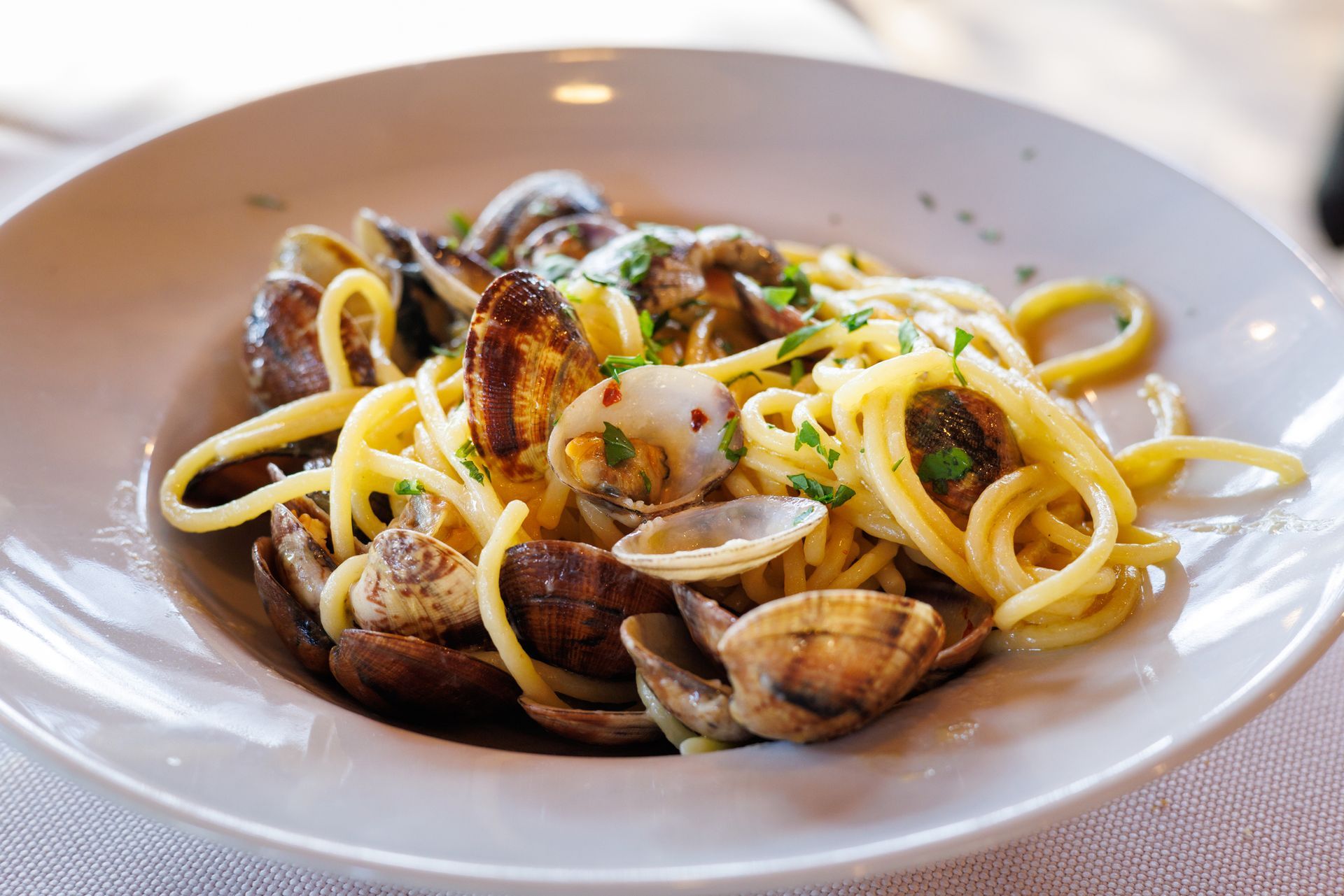 Spaghetti alle vongole in una ciotola bianca, guarnita con prezzemolo e fiocchi di peperoncino rosso.