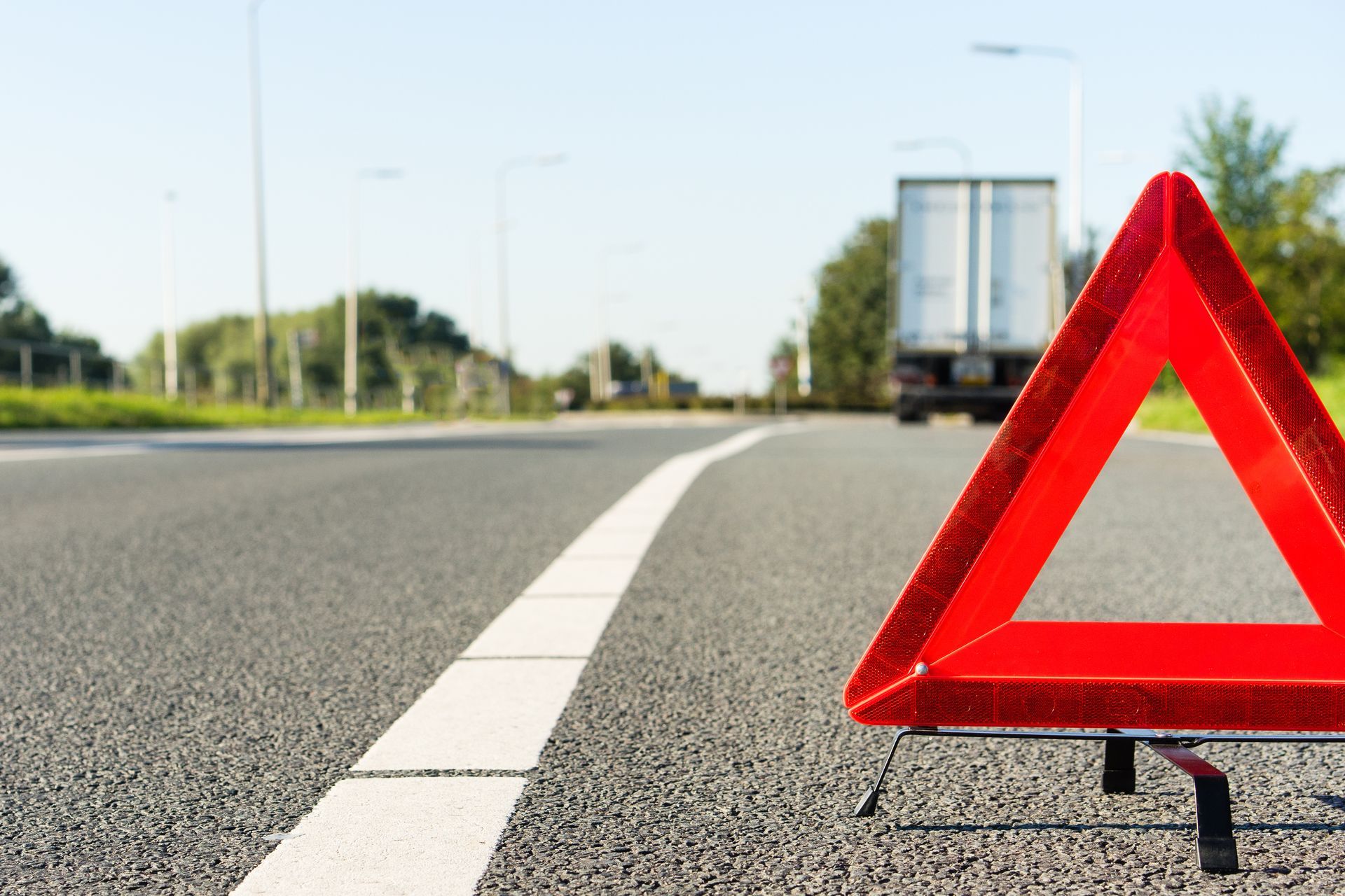 Red warning triangle on the road shoulder with a stopped truck visible ahead in the distance. Red warning triangle on the road shoulder with a stopped truck visible ahead in the distance.