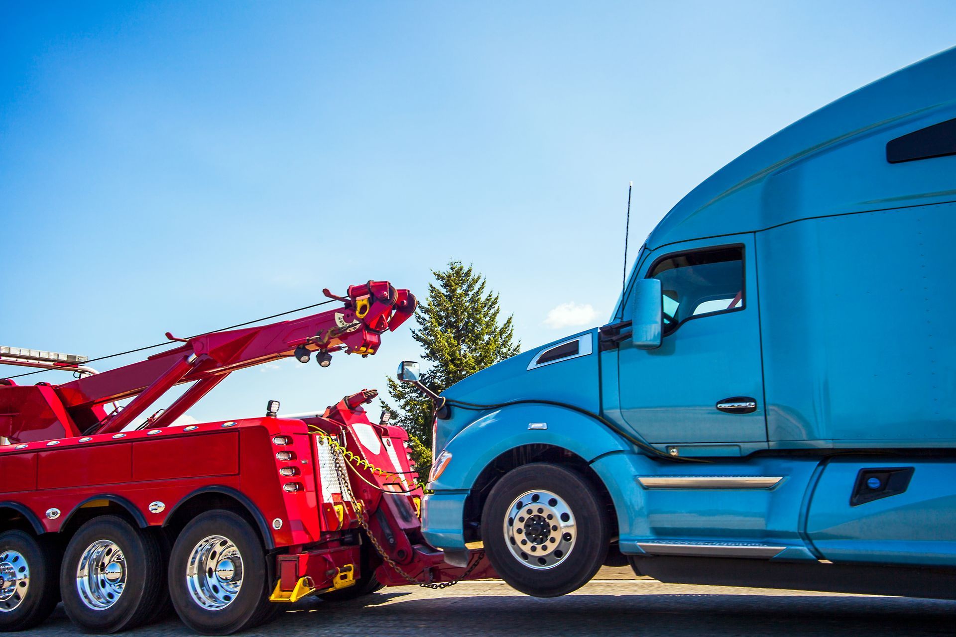 Red tow truck pulling a blue semi-truck under a clear blue sky on a sunny day.