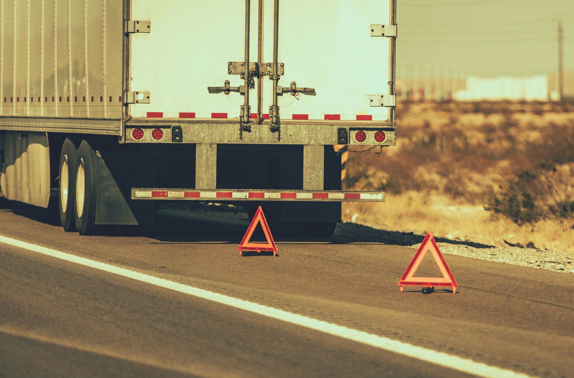 Truck parked on roadside with two orange warning triangles behind it.