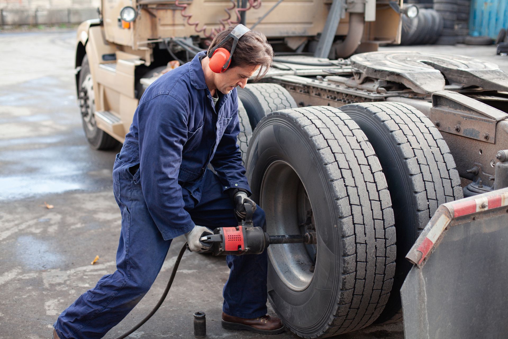 A mechanic using power tools in an auto garage is performing truck repair service on a vehicle.