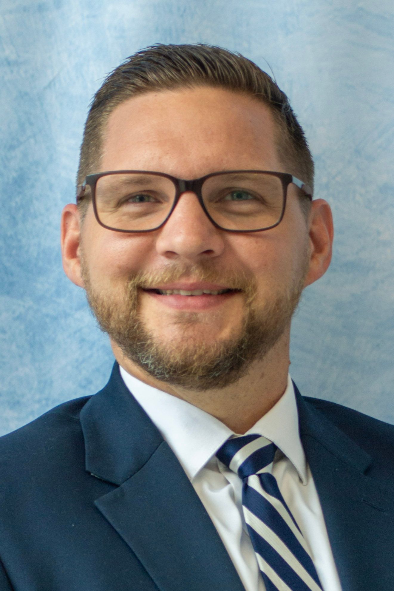 Man in a suit and glasses smiles at the camera.