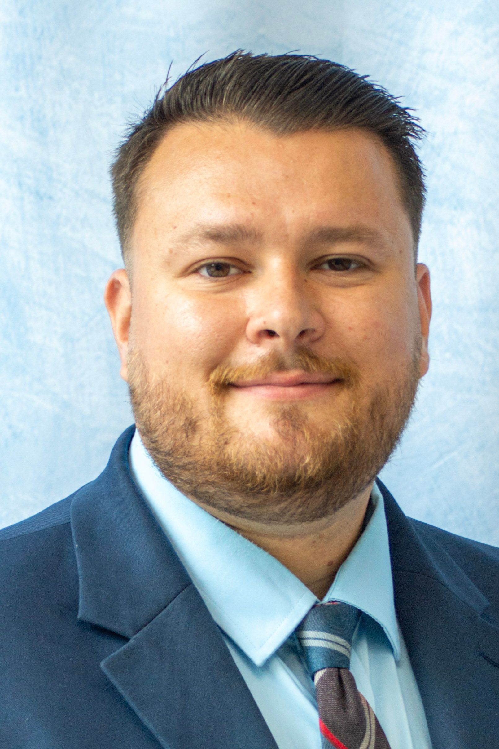 Man in a suit and glasses smiles at the camera.