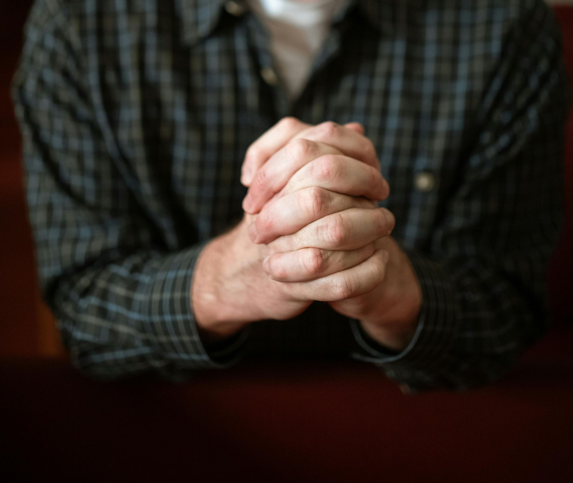 Man with hands clasped in prayer, head bowed, in a room with others.