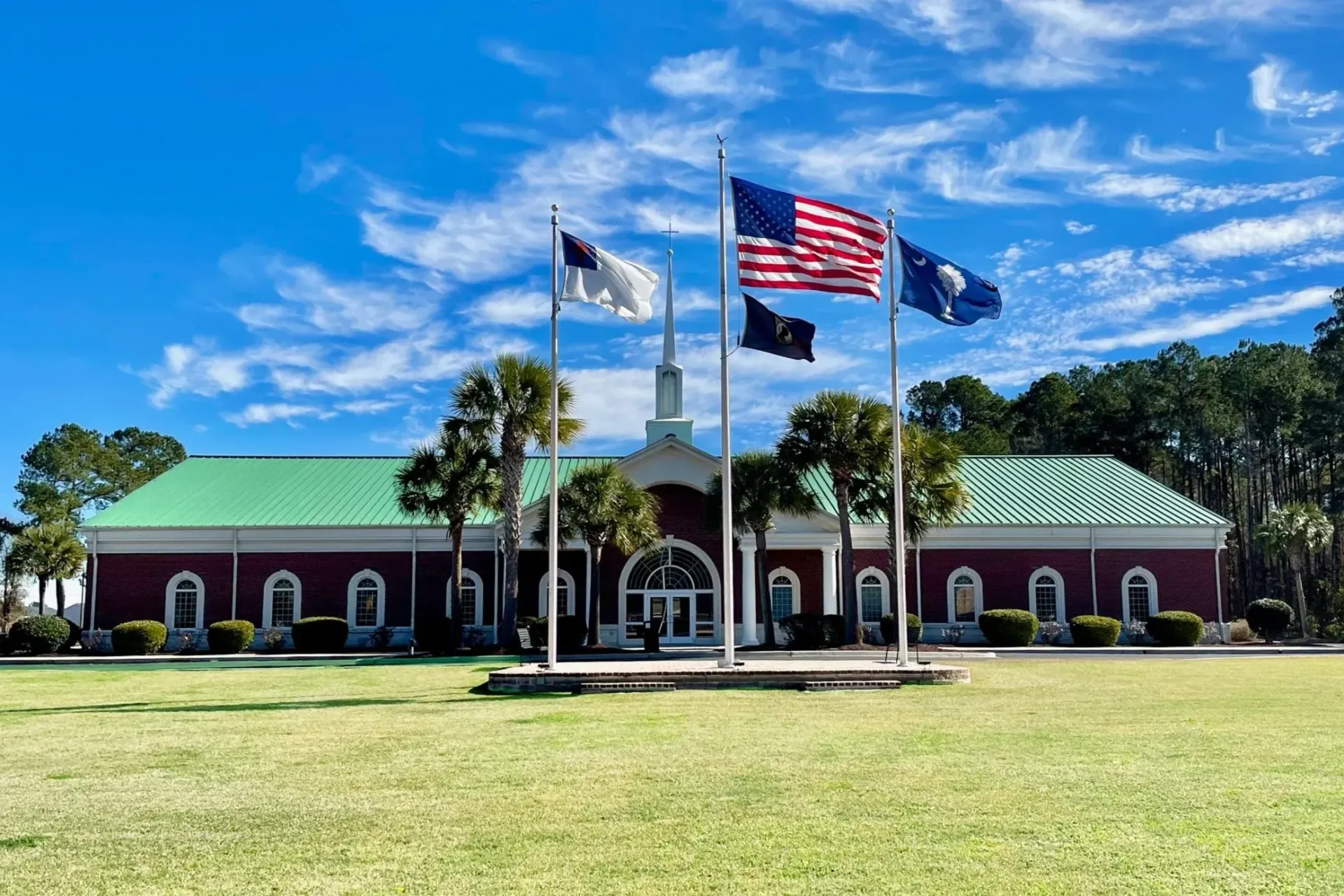 A red brick building with flags, including the American flag, and a grassy lawn under a blue sky.