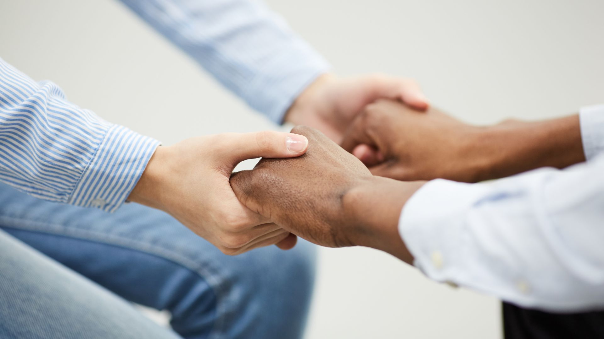 Two people sitting face to face, holding hands in a supportive gesture