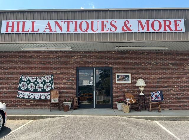 Storefront of “Hill Antiques & More” with brick facade, open door, and antique items displayed outside.