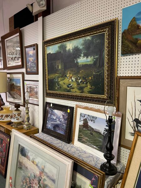 Framed landscape paintings displayed on a pegboard wall in an art shop or gallery.