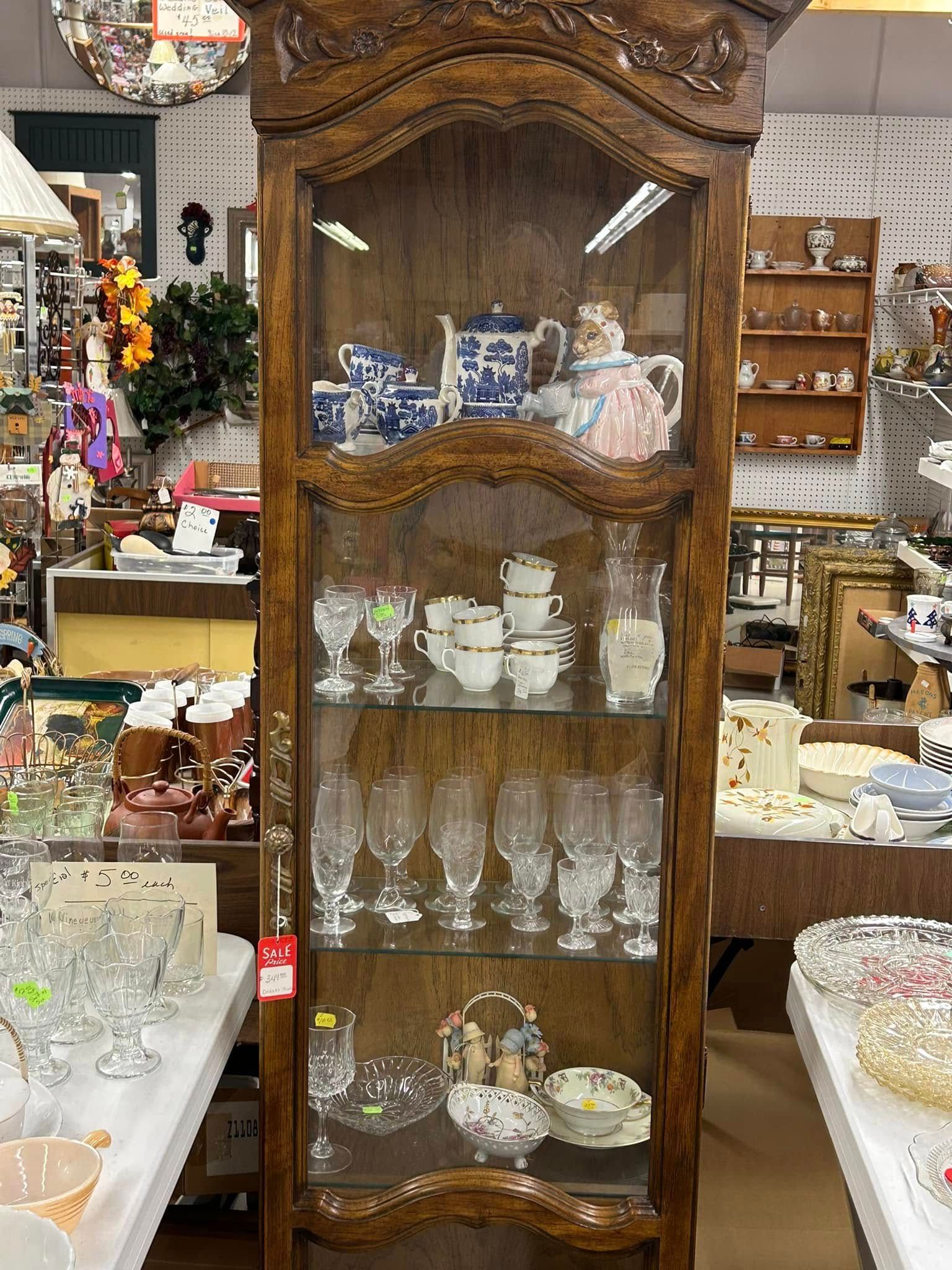 Antique wooden glass cabinet displaying cups, glassware, and dishes in a shop.