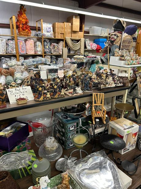 Cluttered shop shelves packed with assorted figurines, jars, glassware, and household items