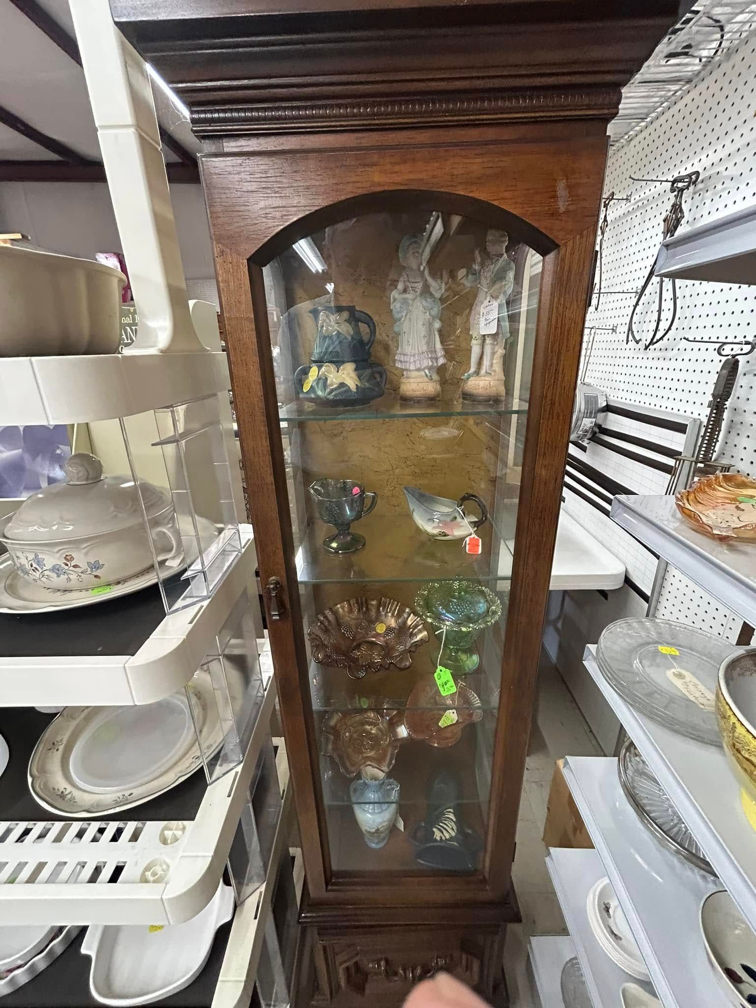 Tall wooden glass cabinet displaying glassware and decor in a store aisle