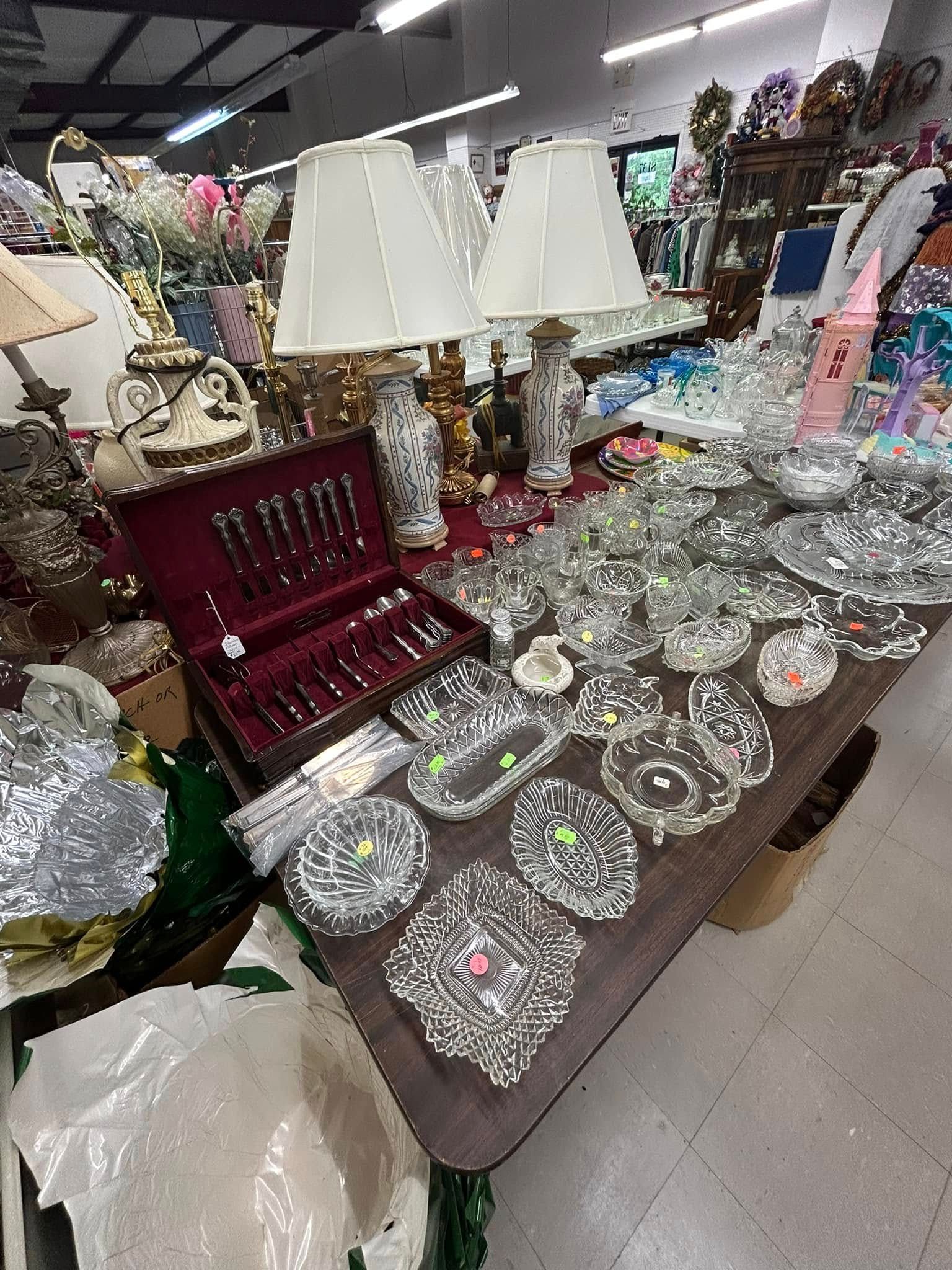 Table of assorted decorative glassware and lamps in a store aisle, with crystal dishes and a red velvet case