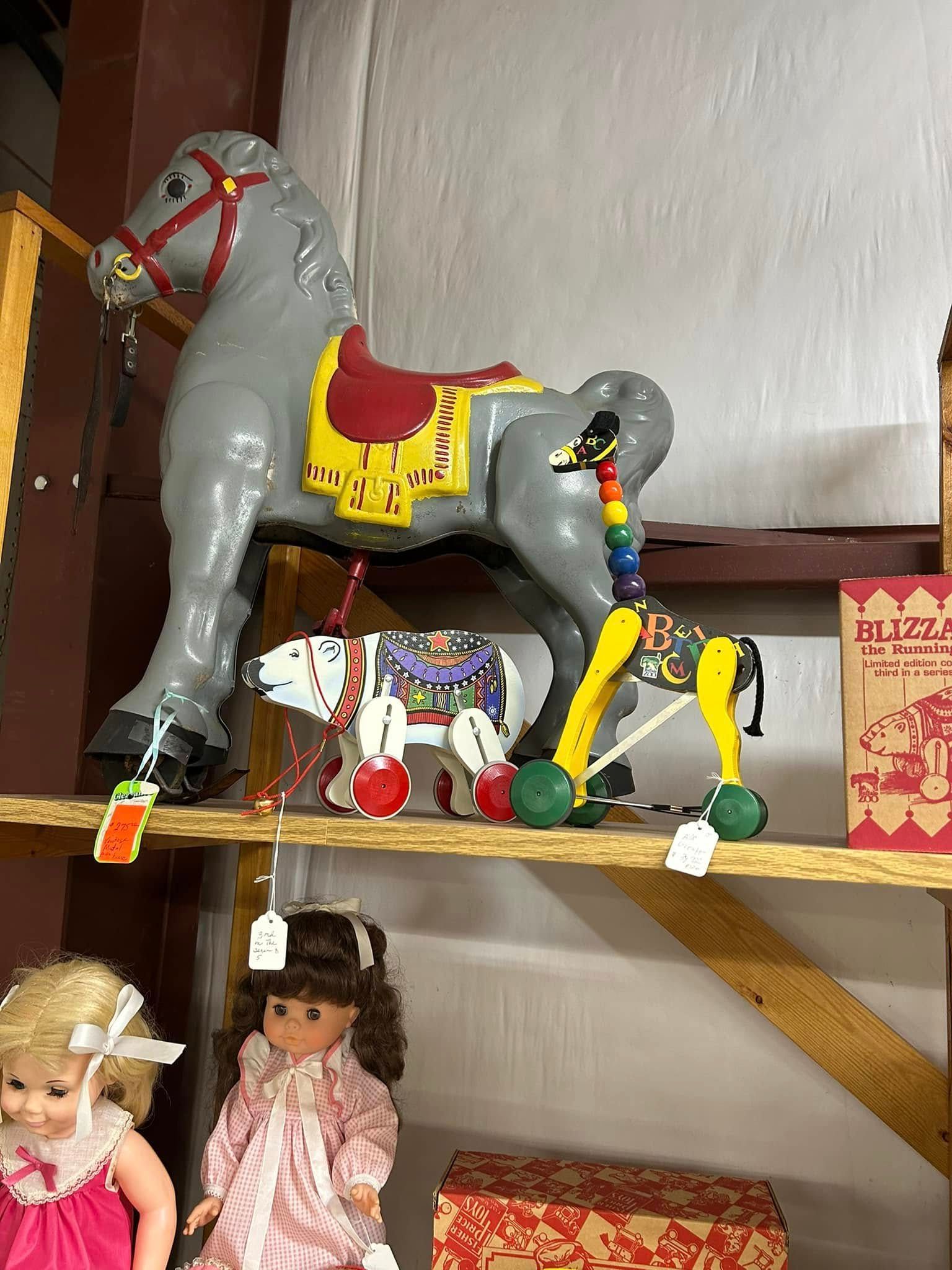 Colorful toy horse display on a shelf with dolls and decorations