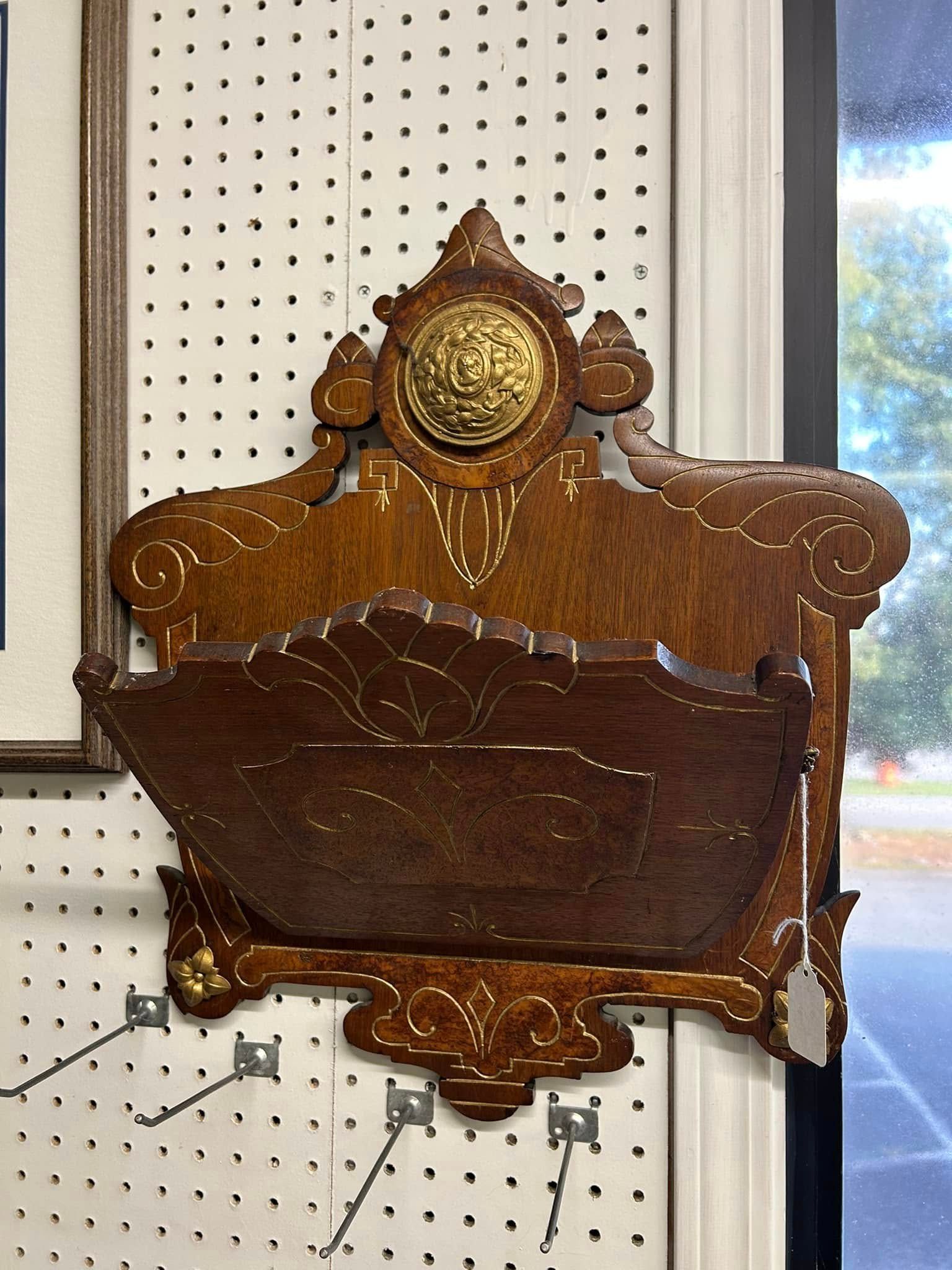 Antique wooden wall-mounted display case with ornate gold trim on a pegboard wall