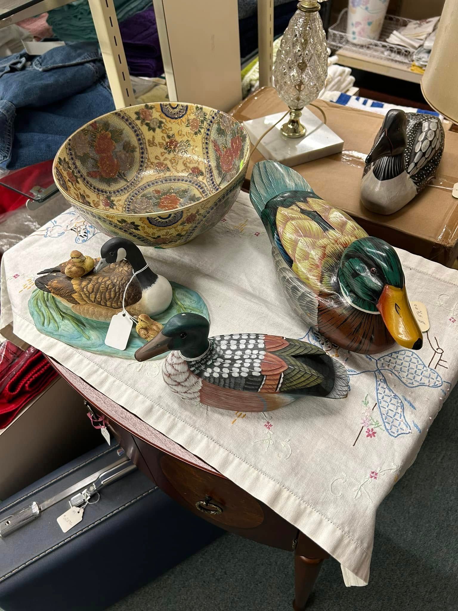 Decorative duck figurines and a patterned bowl displayed on a cloth-covered table in a shop-like setting