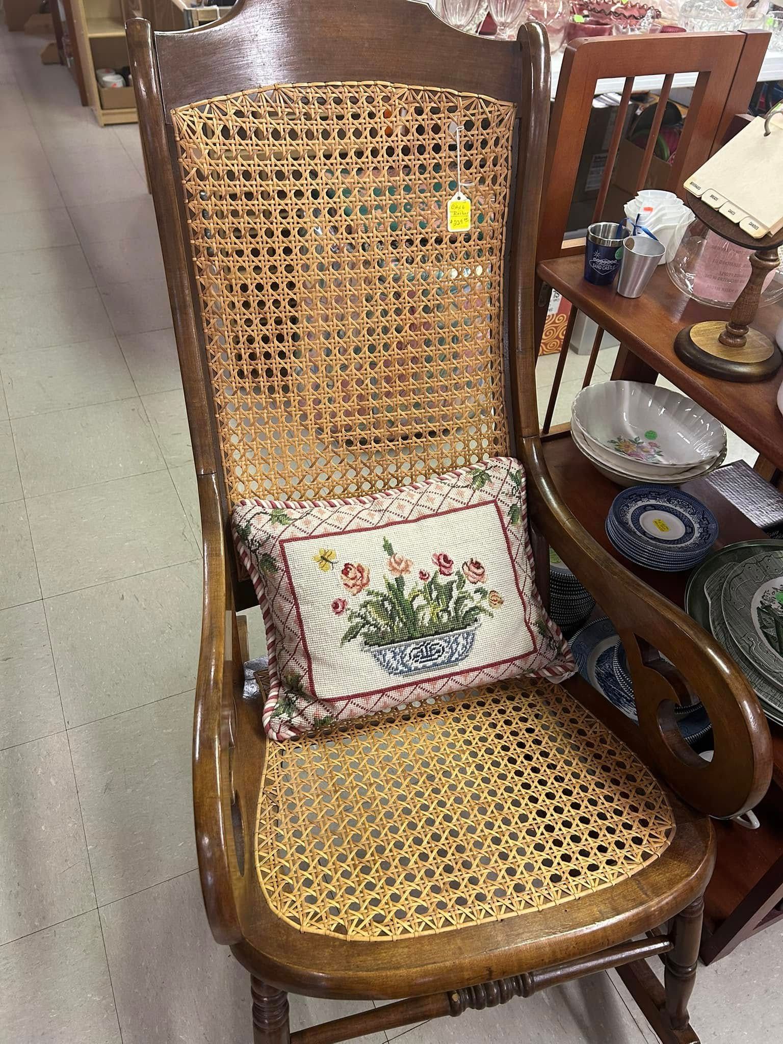 Wicker chair with floral cushion beside a wooden shelf holding dishes and glassware.