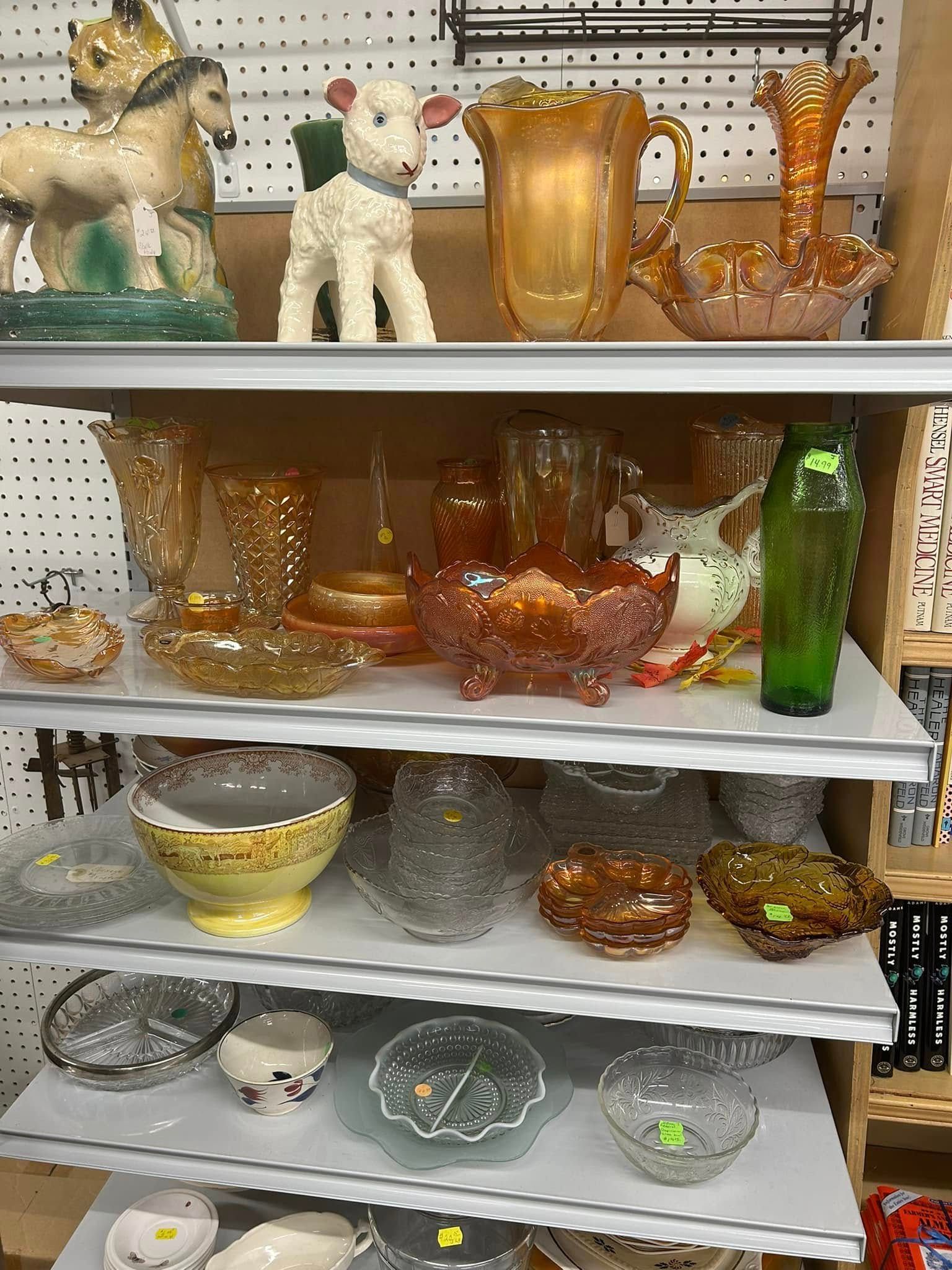 Shelves of assorted glass art vases and dishes in amber, green, and clear colors on display