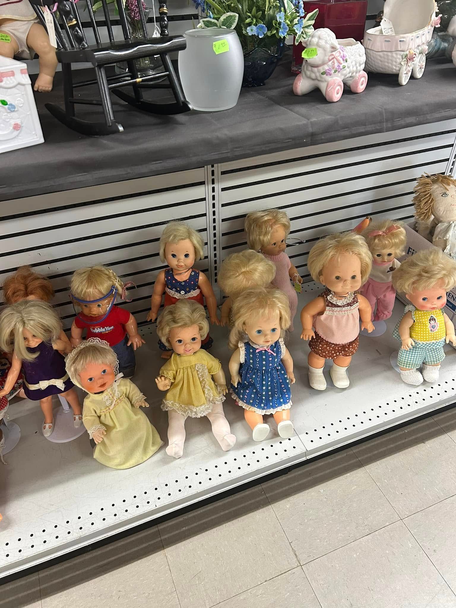 Row of small dolls on a store shelf, dressed in colorful outfits beside a slatted display panel.