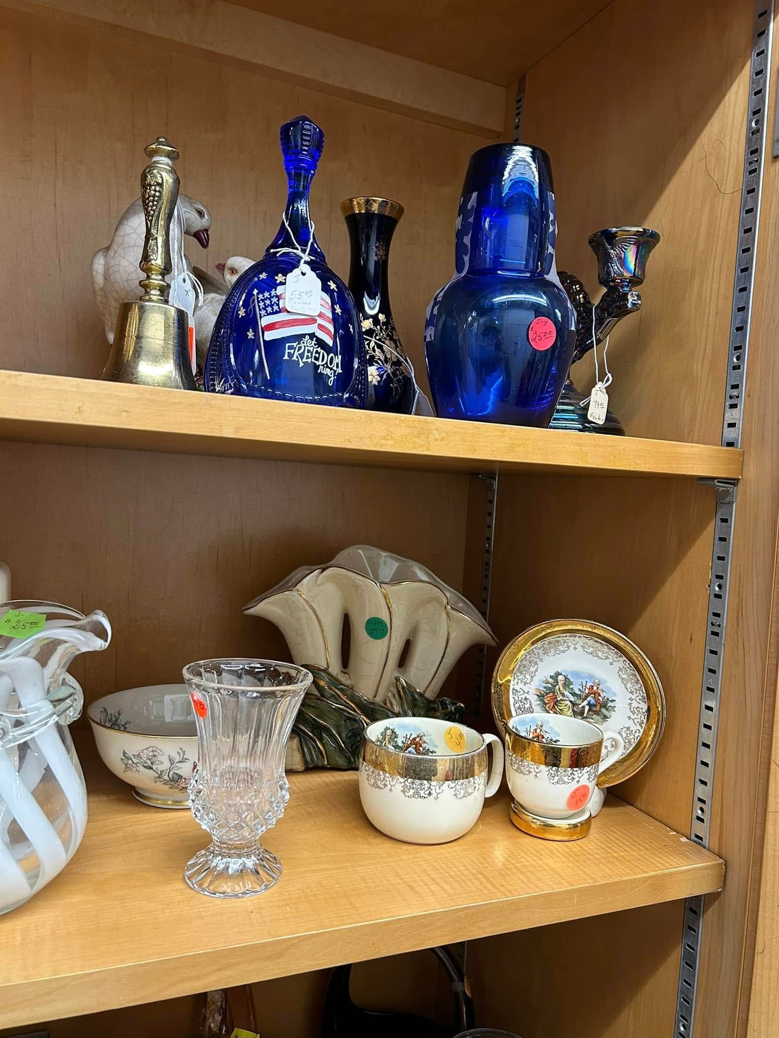 Glass and ceramic figurines and cups displayed on wooden shelves in a cabinet