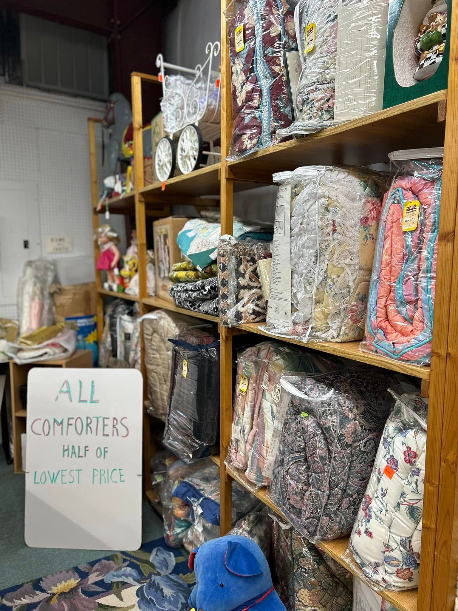 Shelves packed with colorful comforters in a storage room, with a sign reading “All comforters half off.”