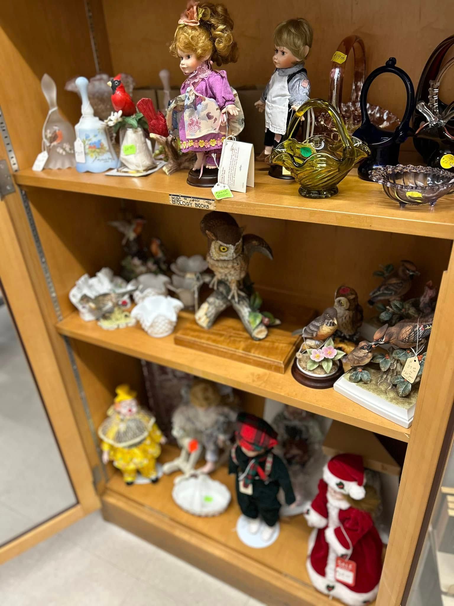Shelves of assorted decorative figurines, including dolls, animals, and Santa figures, displayed in a cabinet