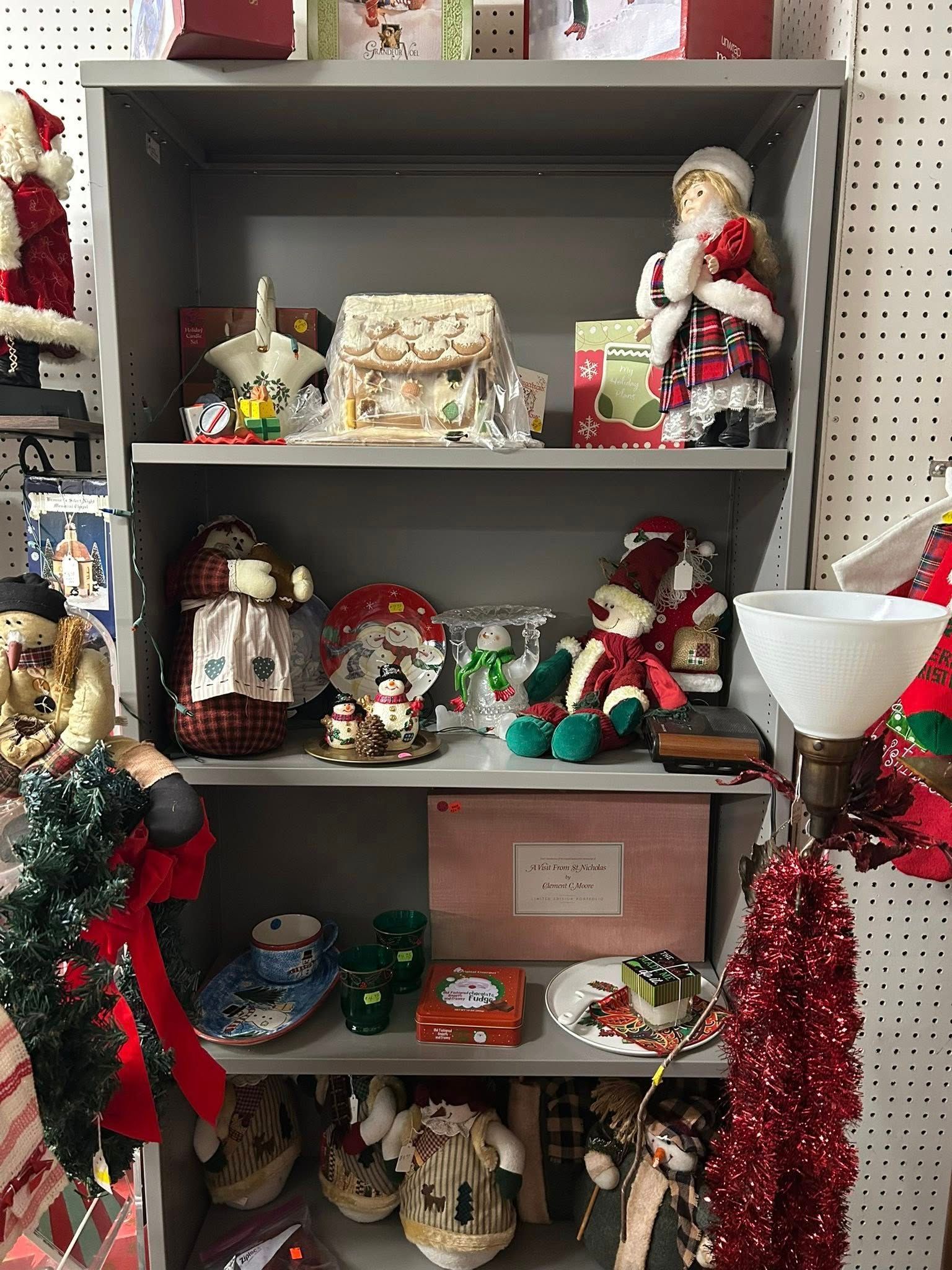 Holiday display on a shelf with Christmas figurines, ornaments, and red tinsel decorations.