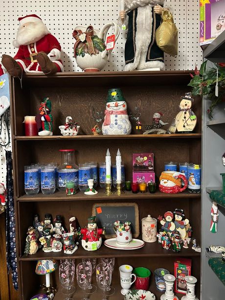 Wooden shelf filled with Christmas figurines, dolls, candles, and holiday decorations