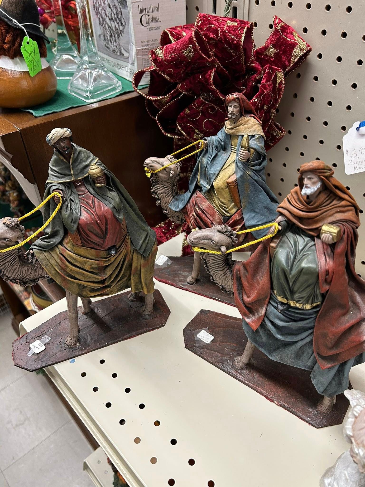 Three miniature medieval figures in colorful cloaks displayed on a pegboard shelf
