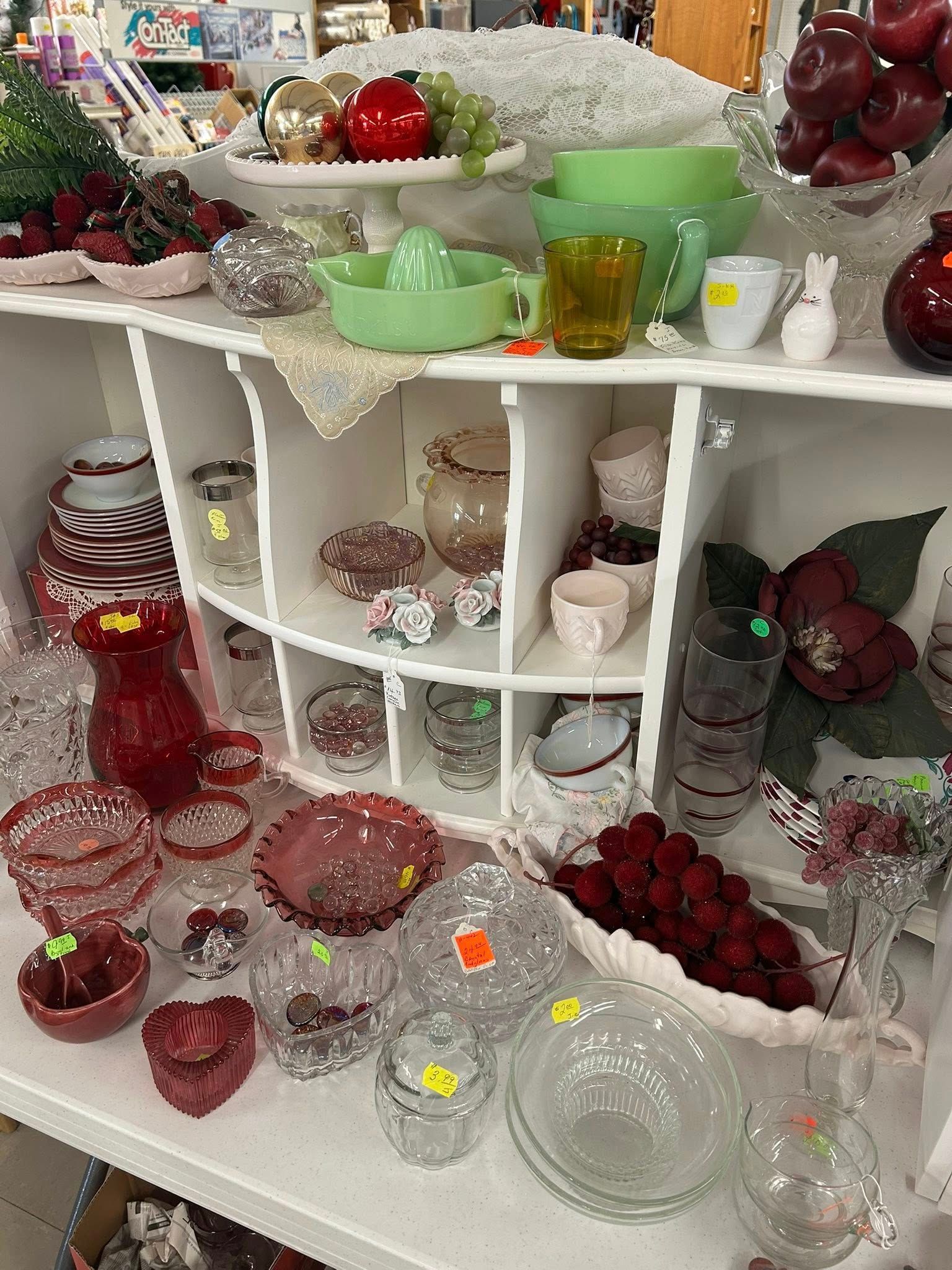 Glassware and decorative dishes displayed on white shelves, with red, green, and clear pieces