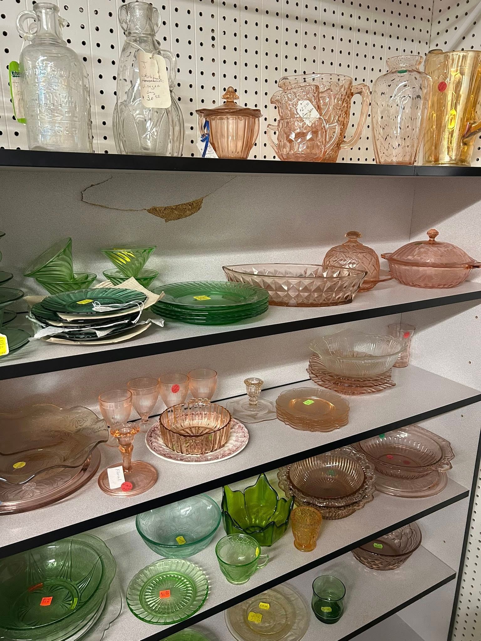 Shelves of assorted decorative glass bowls, vases, and dishes in green, pink, and clear glass.