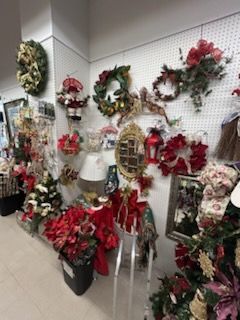 Festive holiday display with ornaments, figurines, framed art, garlands, and a wooden shelf of decorations