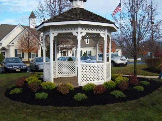 White gazebo in a landscaped yard with cars and houses in the background