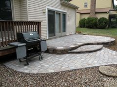 Patio with curved brick steps, black grill, and sliding glass doors beside a house