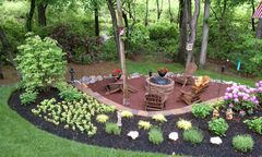Circular garden bed with flowers, trees, and a small stone fountain in a lush green park