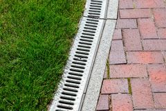Grass beside a concrete drainage grate and red brick walkway